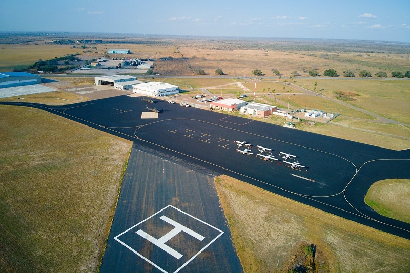 Aerial view of a small airport with several light aircraft parked on a black tarmac.