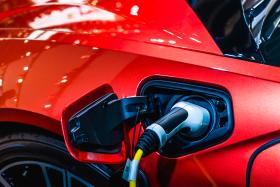 Close-up of a silver electric vehicle charging plug inserted into the charging port of a shiny red car. Close-up of a silver electric vehicle charging plug inserted into the charging port of a shiny red car.