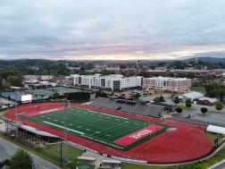 Aerial view of Barron Stadium and the surrounding River District in Rome, Georgia, at sunrise, showcasing the athletic field, downtown area, and scenic hills.