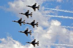 Six F-16 fighter jets fly in formation against a cloudy blue sky, trailing white smoke. Six F-16 fighter jets fly in formation against a cloudy blue sky, trailing white smoke.
