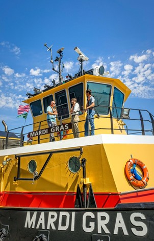 From left, Jeff Guilott with Cooper T. Smith; Justin Ehrenwerth, president and CEO of The Water Institute of the Gulf; and Andrew Courtois, field geologist with The Water Institute of the Gulf discuss how sensors measuring the Mississippi River depth are integrated into the tugboat’s systems. (Photo by Tim Mueller, Tim Mueller Photography)